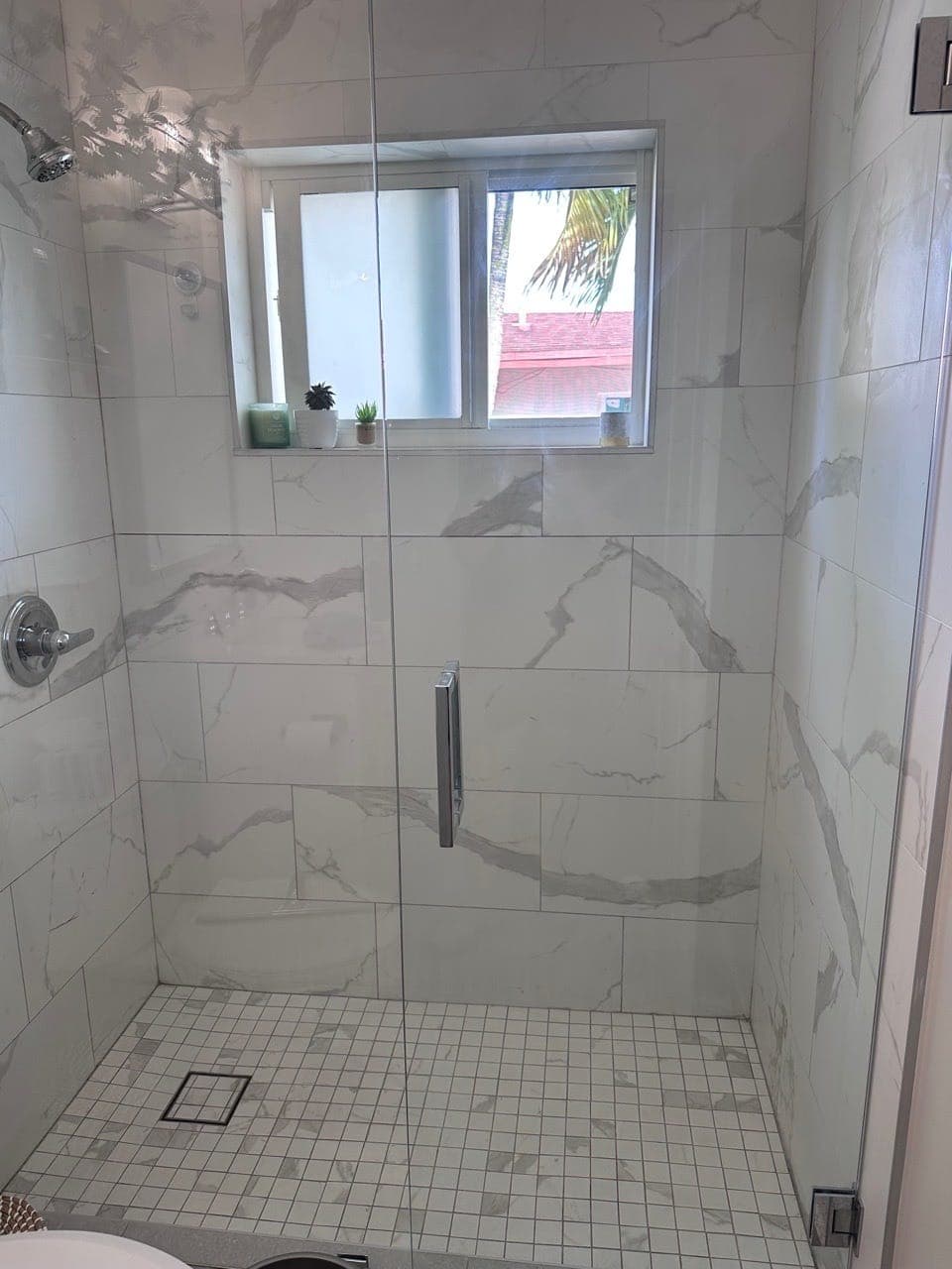 A frameless glass shower with white marble-look tile and a clean tile floor