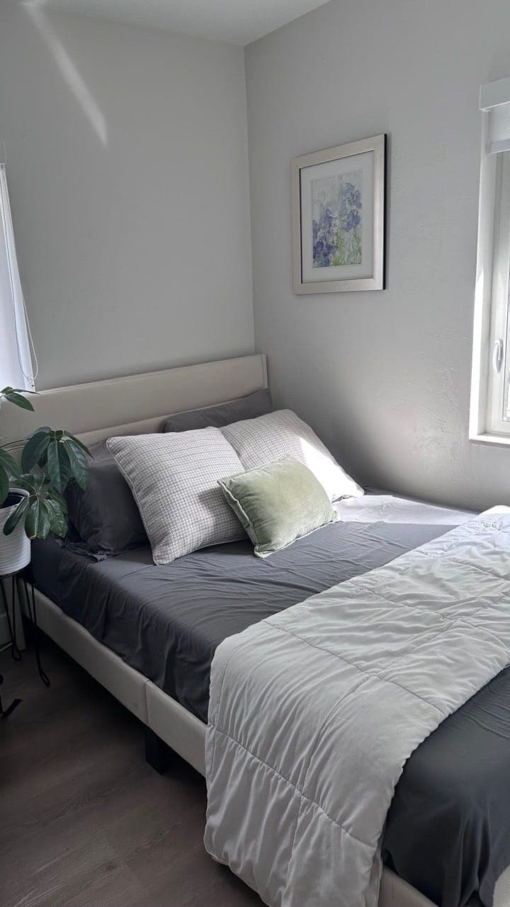 A made bed with grey and white covers in a bright bedroom