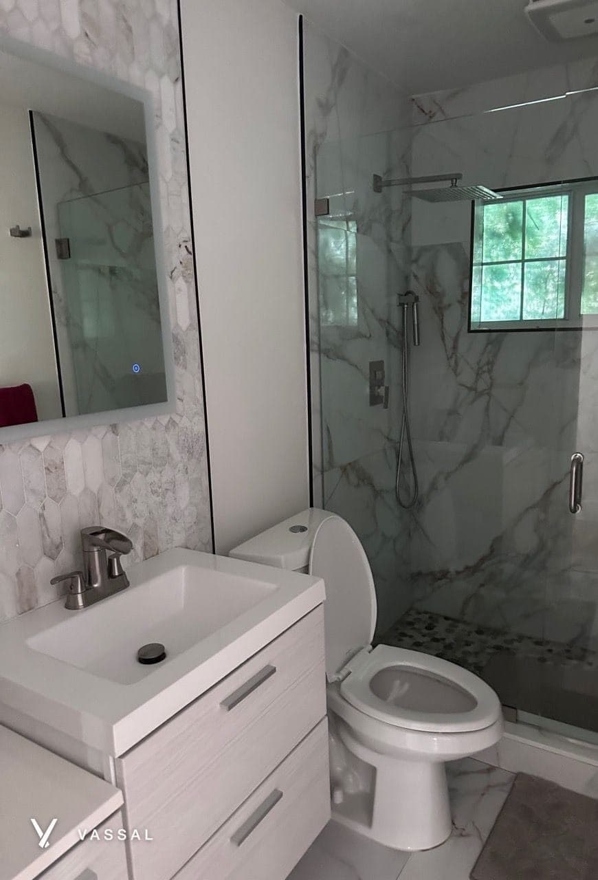 A bathroom with a marble-look glass shower, a white vanity and a toilet