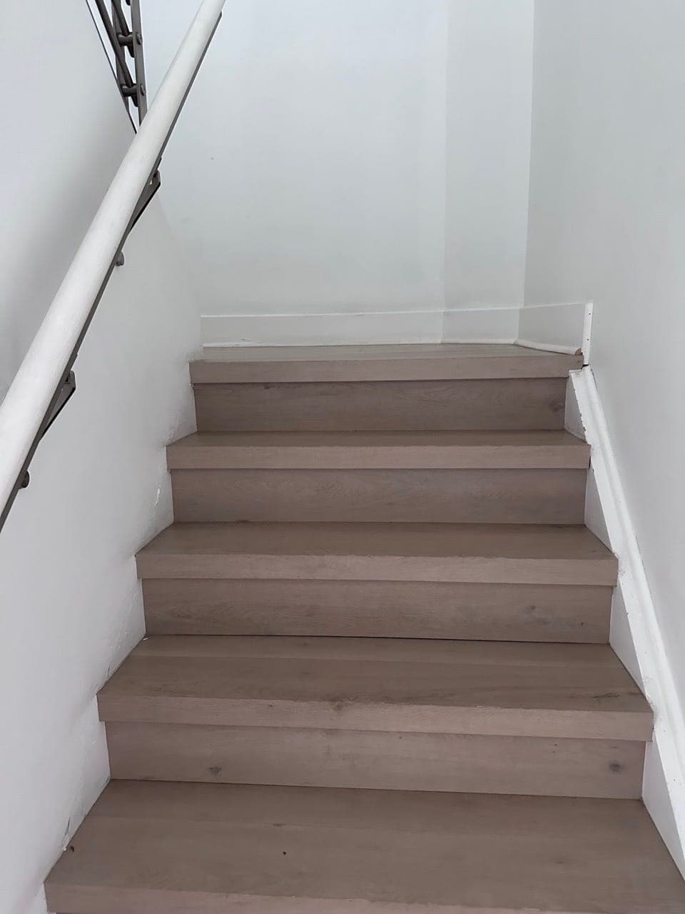 A staircase with clean wood treads and a white rail