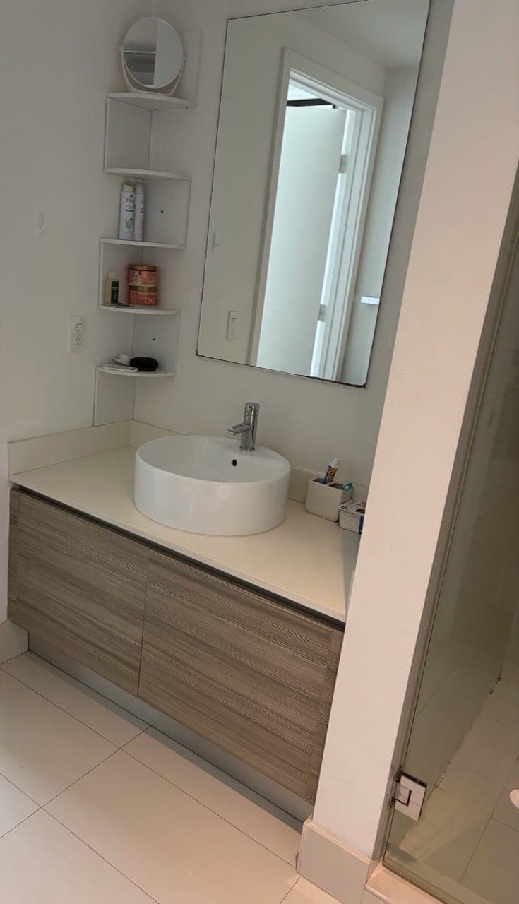 A wood vanity with a white vessel sink under a tall mirror