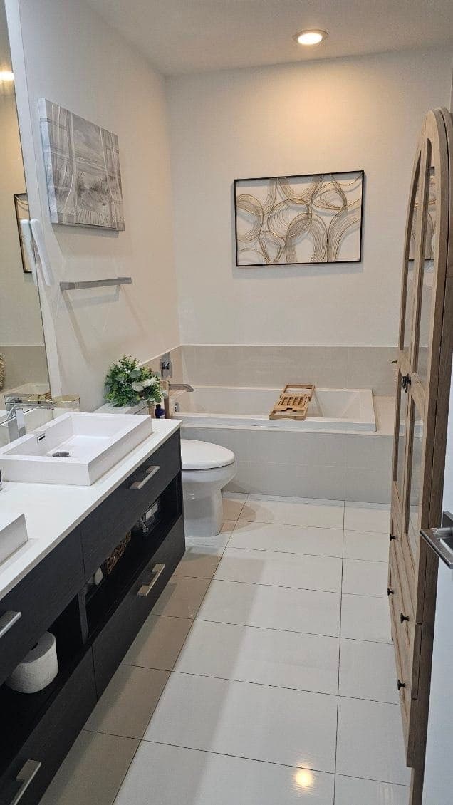 A bright bathroom with a white tub, a vanity sink and a white tile floor
