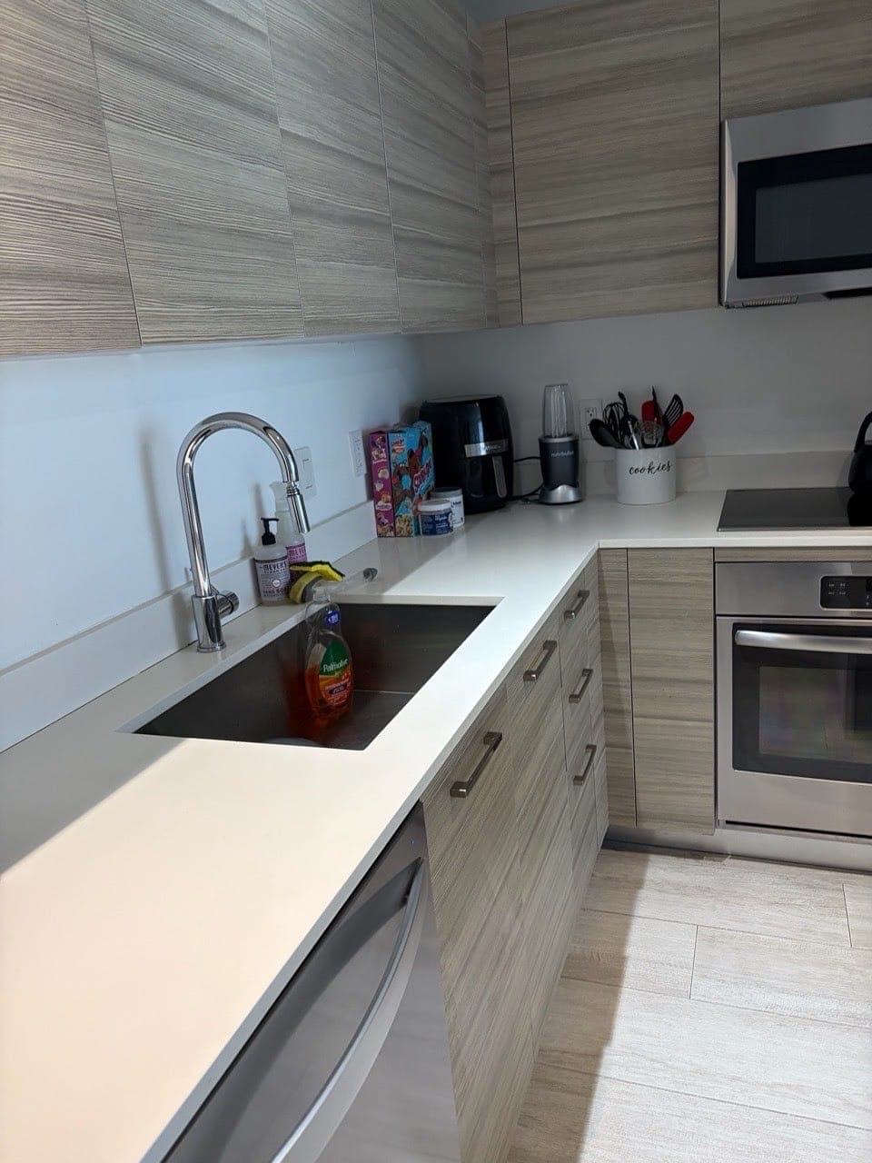 A kitchen with white counters, a wiped sink, wood cabinets and stainless steel appliances