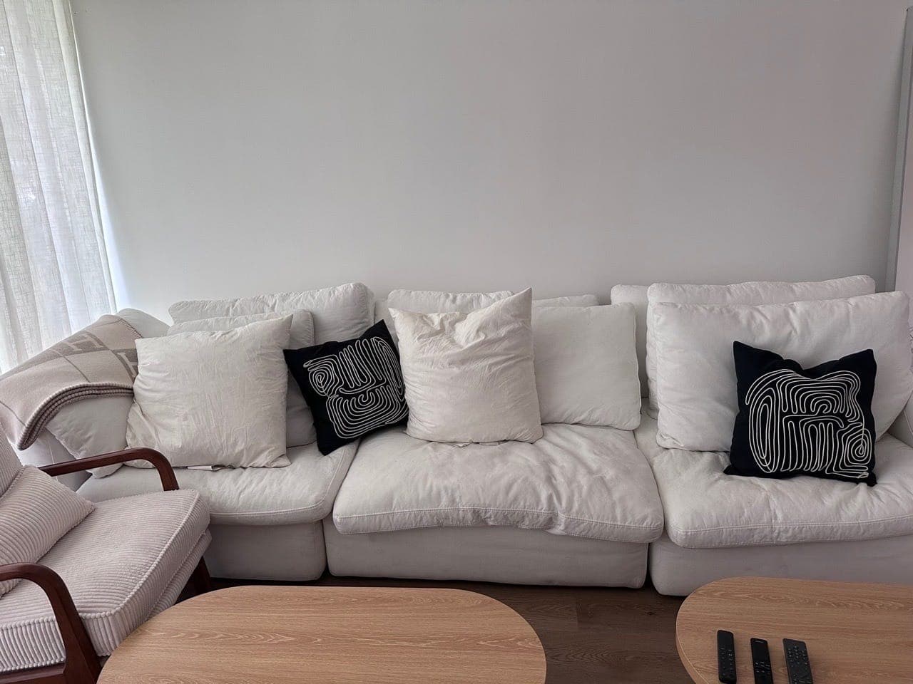 A white sofa with its cushions set beside two round wooden tables